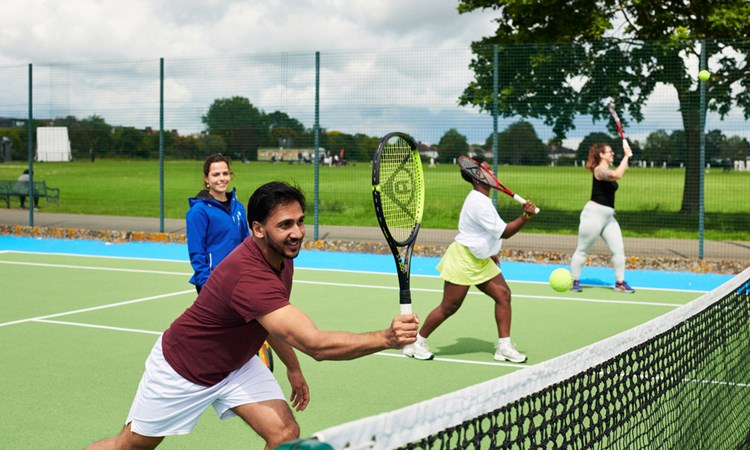 A first time tennis player practicing making a shot at the net alongside two other people.