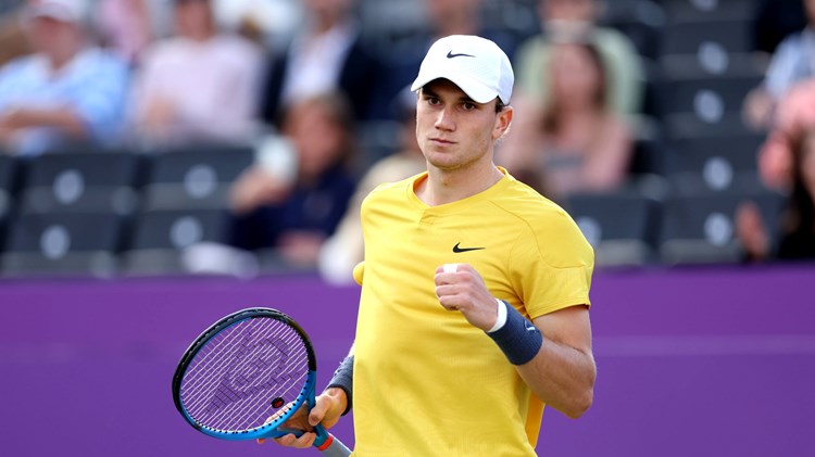 Jack draper wearing a yellow shirt and white hat clenching his fist on court at the cinch Championships while holding his tennis racket