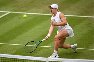 Sonay Kartal crouching down to hit a volley at the net on a grass court at Wimbledon