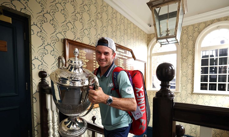 Tommy Paul walking up the stairs at the Queen's Club while carrying his trophy and smiling